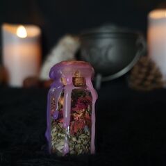 Mini spell jar for empowerment - jar is clear glass containing a mix of herbs and crystals, topped with a cork stopper and sealed with purple and pink wax which drips down the sides of the jar